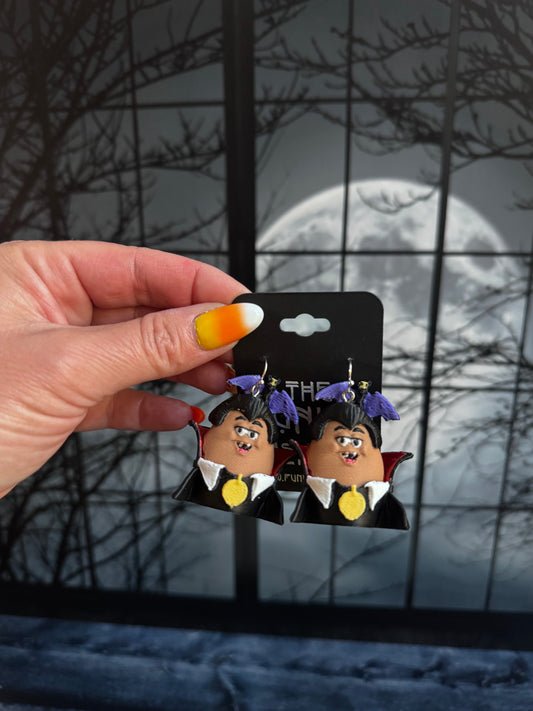 Handmade vampire nugget buddy dangle earrings with purple hair, a black high collar cape and a gold medallion